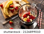 Preparing strawberry and banana smoothie in mixer on wooden table