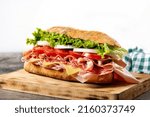 Small photo of Submarine sandwich with ham, cheese, lettuce, tomatoes,onion, mortadella and sausage on wooden table