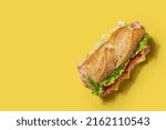 Small photo of Submarine sandwich with ham, cheese, lettuce, tomatoes,onion, mortadella and sausage on yellow background. Top view. Copy space