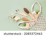 Small photo of Eco shopping of personal care zero waste supplies: wooden comb, brush, toothbrush, soap in handmade eco bag with a paper tag on green background. Woven DIY mesh reusable shopper. Plastic-free concept