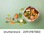 Small photo of Sorted kitchen waste in paper eco bag on green background. Compost-container. Sustainable life style. Vegetable and fruit peels, scraps from food preparation collected in trash-pack for recycling