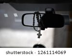 A rosary with a christian cross hangs on a car mirror.