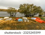 Small photo of A row of colourful upturned rowing boats under the trees on the shore of Lake McGregor