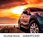 Blue luxury SUV car parked on concrete road by sea beach with beautiful red sunset sky. Summer vacation at tropical beach. Road trip. Front view sports and modern design SUV car. Summer travel by car.