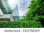 Small photo of Sustainble green building. Eco-friendly building in modern city. Sustainable glass office building with tree for reducing carbon dioxide. Office with green environment. Corporate building reduce CO2.