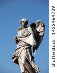 Small photo of A detail of the Angel with the sudarium, the cloth used to wipe the face of Christ, on the Ponte Sant'Angelo. The baroque statue can be seen against a deep blue summer sky.