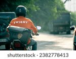 Small photo of Bangalore, India - 7th Oct 2023: Swiggy food delivery startup technology startup rider courier riding at sunrise sunset showing the long hours these gig workers keep
