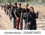 Small photo of Eagle Pass, TX, USA - Sept. 20, 2023: A group of migrants seeking U.S. asylum walk down a road beside the Rio Grande River to turn themselves in to the Border Patrol.