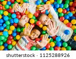 Above view portrait of three happy little kids in ball pit smiling at camera raising hands while having fun in children play center, copy space