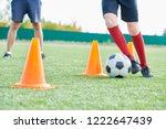 Low section portrait junior football team training outdoors in sunlight with focus on  unrecognizable boy leading ball between orange cones, copy space