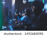 Group of serious gloomy young hackers in hoodies sitting in row and typing on keyboards fastly in server room