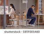 Small photo of Side view portrait of two people wearing masks in office while working at desks in separate cubicles post pandemic, copy space