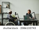 Portrait of African-American person with disability speaking to microphone while recording podcast in studio