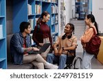 Small photo of Diverse group of students with young man in wheelchair chatting cheerfully in college library, inclusivity concept