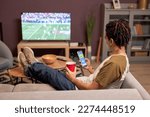 Back view at young man watching football match at home and relaxing on couch with online betting app