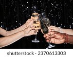 Closeup of hands toasting with champagne glasses at party against glittering background with confetti
