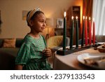 Small photo of Dreamy smile Black girl looking at colorful candles representing struggle, hope and heritage