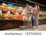 Full length portrait of happy young family shopping for groceries in supermarket together with little boy, while choosing fresh bread loaf in bakery department