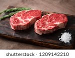 Two fresh raw rib-eye steak on wooden Board on wooden background with salt, pepper and rosmary in a rustic style