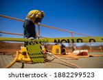 Small photo of Safety workplace yellow striped caution tape warning sign barricade exclusion zone preventing from public access while defocused construction worker welder welding repairing fence