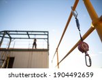 Small photo of Safe work practices an inertia reel shock absorbing fall protection hook lanyard device clipping hanging on handrail with defocused construction worker working at heights in fall restraint background