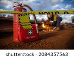 Small photo of Safety workplace yellow striped caution tape warning sign barricade exclusion zone preventing from public access first aid kit with fire extinguisher defocused construction worker using oxy hot work