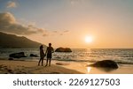 Small photo of A couple of men and women watching the sunset o a tropical beach at the Seychelles Islands.
