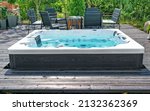 Small photo of Large hot tub embedded in the backyard terrace. A sunny summer's day in the shelter of a green garden. Everyday luxury and relaxation in your own backyard. Spa complex, vacation and traveling concept.