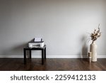 Small photo of Inkjet printed on small black table in an empty room. Dry flower arrangement in tall clay vase next to large candle placed on laminated floor and white wall of the interior.