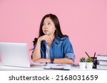 Young successful business woman wearing a casual shirt. She is sitting on her desk thinking something on a pink background.