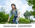 Small photo of Happy Asian woman wearing a helmet and listening to her favorite music while riding a bicycle through a city park.