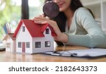 Small photo of Businesswoman looking at house model through magnifying glass. Real estate appraisal, land valuation and house selection concept.