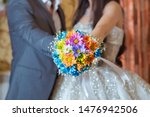 Coloured macro photo of a detailed bouquet with colorfull roses, white small flowers and a fake diamond in the centre of the rose . He holds a wedding flower in his hand