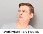 Small photo of Studio close-up portrait of funny blond mature man grimacing from displeasure, disgust and squeamishness, sniffing nasty stinky smell, seeing something repulsive. Headshot over gray background