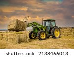 A ranch worker moving bales of...