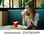 Small photo of Woman has breakfast in Mcdonald's restaurant. Female eating eating hamburger and french fries in Mccafe. Fast food nutrition. Wroclaw, Poland - July 2, 2023