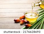 Small photo of Pouring palm oil into glass bowl with fresh palm nuts on wooden table.