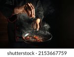 Small photo of Professional chef adds salt to a steaming hot pan. Grande cuisine idea for a hotel with advertising space.