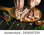 Small photo of Cooking a meat dish. The cook cuts the meat brawn with a knife on a kitchen cutting board. Close-up of a chef hands while working.