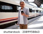 Happy senior man waiting a train. Man using the phone while waiting a train