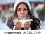 Winter. Woman with wearing ear muffs blowing on snow in hands, Girl in the park in winter blowing snowflakes	