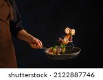 Cooking seafood - shrimp, octopus with vegetables in a frying pan on a black background by a professional chef. Frozen in-flight food. Sea food. Vegetarian, diet food. Banner.