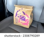 Small photo of Seattle, WA USA - circa March 2023: Close up view of a Taco Bell fast food bag inside of a car.