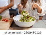 Female hands mixing green salad in the bowl with forks