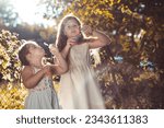 Small photo of Two little girls, sisters outdoors in white dresses, making soap babbles