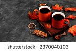Small photo of Two colored red and yellow enamel mugs with hot autumn drink, mulled wine with apples and cinnamon and autumn fallen leaves on a rusty table, seasonal banner or advertisement, hello autumn concept