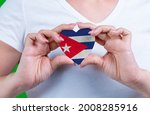 Woman in white t-shirt holds a heart in the form flag Cuba on her chest. Photo for a postcard on Flag Day, Independence Day, travel, patriotism, other holiday