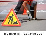 Small photo of Road works sign, worker of municipal services repairs drainage system. Wastewater treatment, orange roadblock cones on the city street