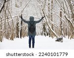Woman wearing down jacket standing with her hands raised and enjoying the snowy weather. Leisure in winter park, cold season