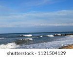 Small photo of A beach with waves coming in on a cloudy day with a deep blue sky in the background. There is a break water in the background.